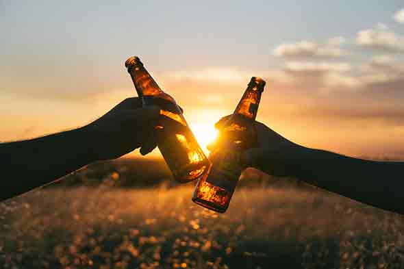  A photo of two people holding beer bottles with the sunset in the background