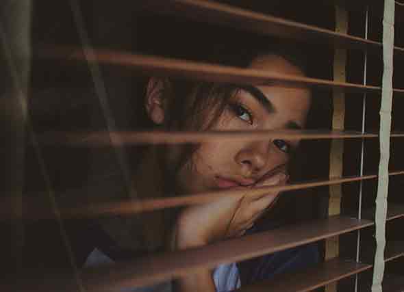 woman looking through window blinds