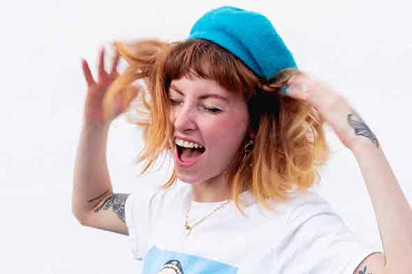 A woman in a white printed shirt with a blue cap screaming and ruffling her hair.