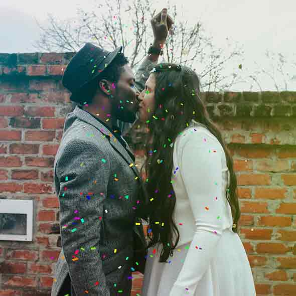 An interracial couple kissing with confetti falling around them.